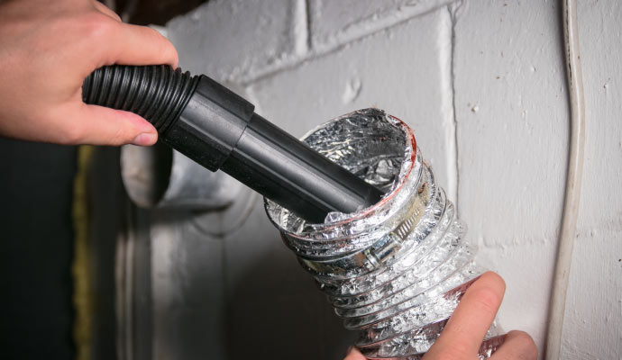 A person cleaning a dryer vent with a vacuum cleaner hose