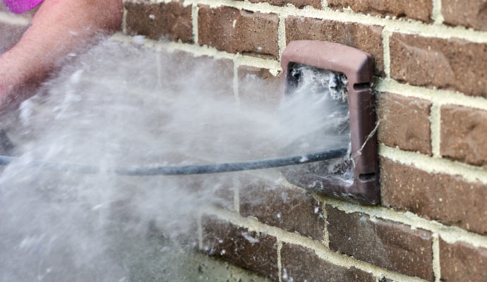 A person cleaning a dryer vent with a hose