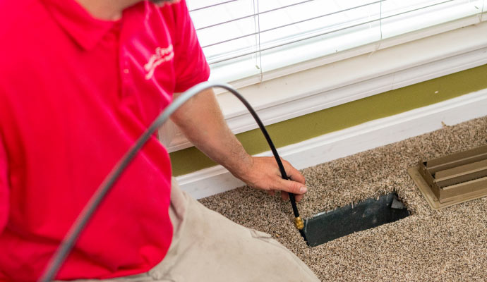 A person cleaning an HVAC vent on a carpeted floor