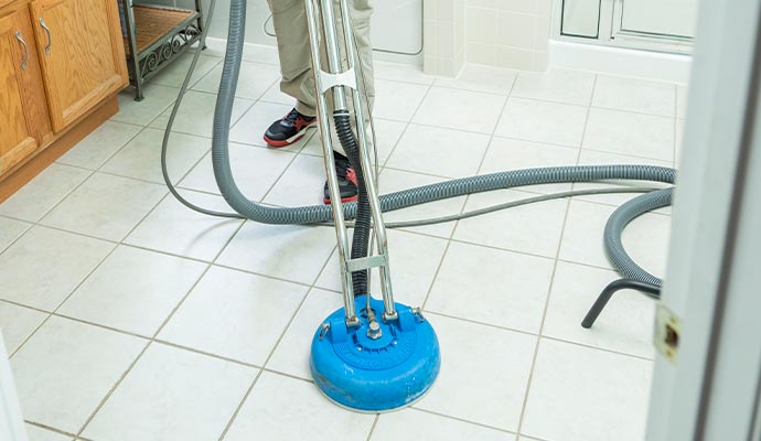 person cleaning tiled floor with scrubber