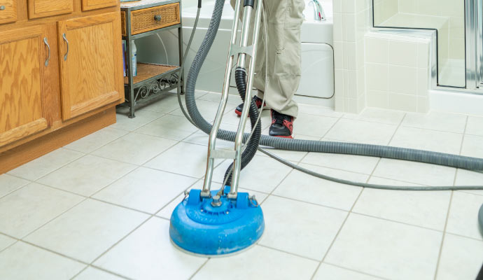 A person cleaning a tiled floor with a cleaning machine