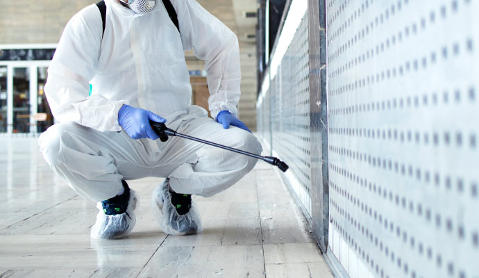 Individual in protective suit using disinfection spray equipment.